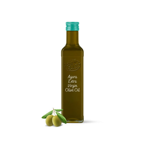 Extra virgin Agora olive oil in a glass bottle with a teal cap, accompanied by fresh green olives and leaves.