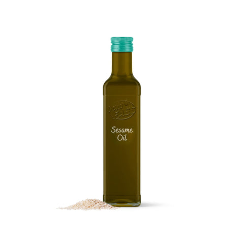 Sesame oil in a tall, amber-colored bottle with a green cap, next to a small pile of sesame seeds.