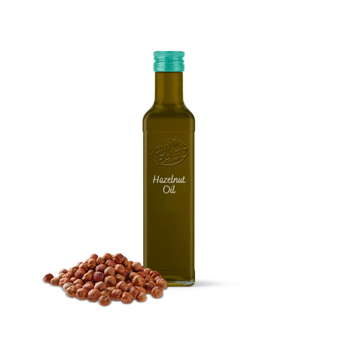 Hazelnut oil in a sleek, tinted glass bottle with a green cap, placed beside a pile of whole hazelnuts.